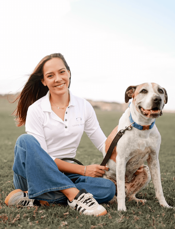 Anayla Fontán Núñez kneeling in a grassy field beside a happy white Golden Retriever, with a Puerto Rico fort tower visible in the distance
